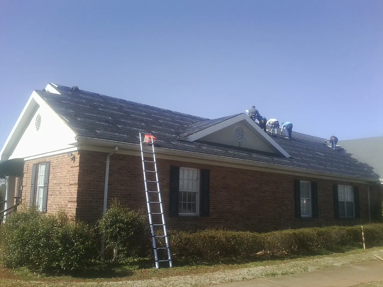 Crew tearing shingles off a brick ranch roof with a ladder set — Emergency Roof Repair work by our crew in Nelson
