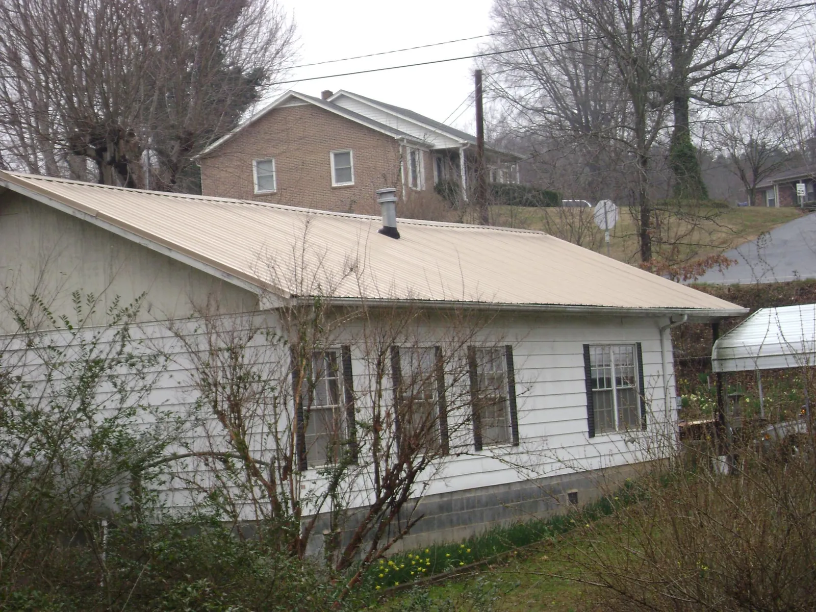 Tan metal roof on a white sided house set into a hillside — Commercial Roofing by Roofing Brothers in Nelson